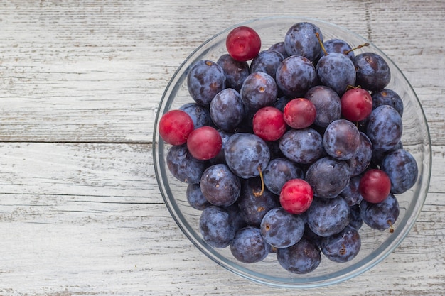 Fresh plums in cup on white wooden table