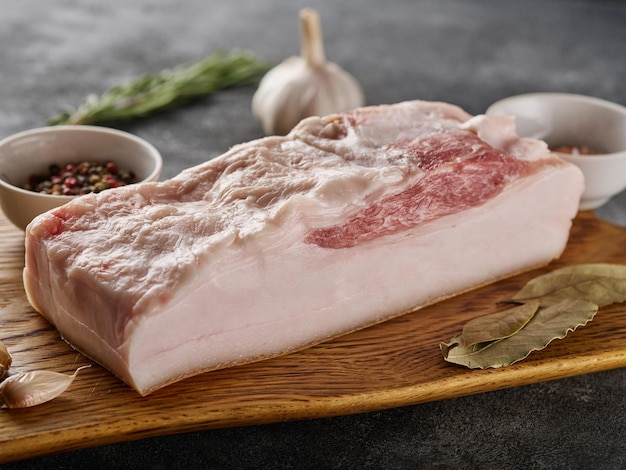 Fresh pork belly block on wooden board with salt and pepper closeup