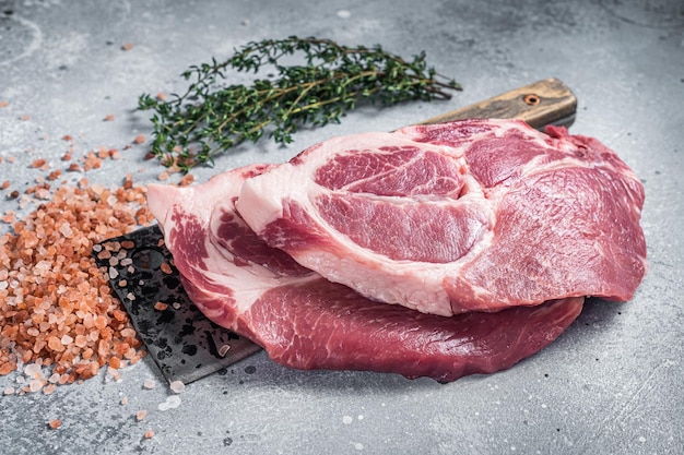 Fresh pork tender steaks from raw neck meat on butcher meat cleaver with salt and thyme. Gray background. Top view.