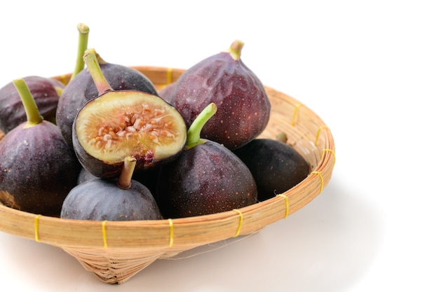 Fresh purple fig fruit and slices in bamboo basket isolated on white background