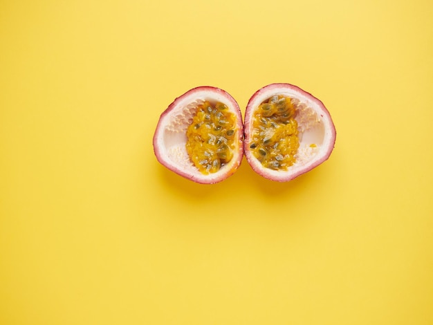 Fresh purple passion fruit halved with yellow gelatinous pulp and seeds Top view symmetrical composition on yellow background