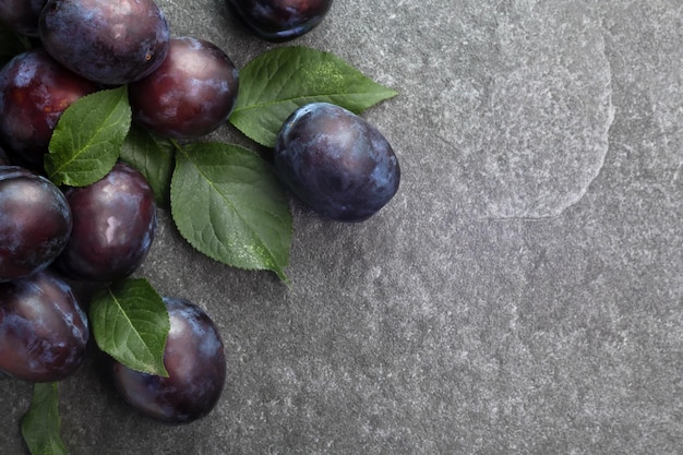 Fresh purple plums with leaves on stone top view copy space