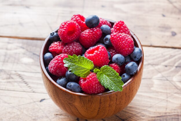 Fresh raspberries and blueberries in a wooden plate.