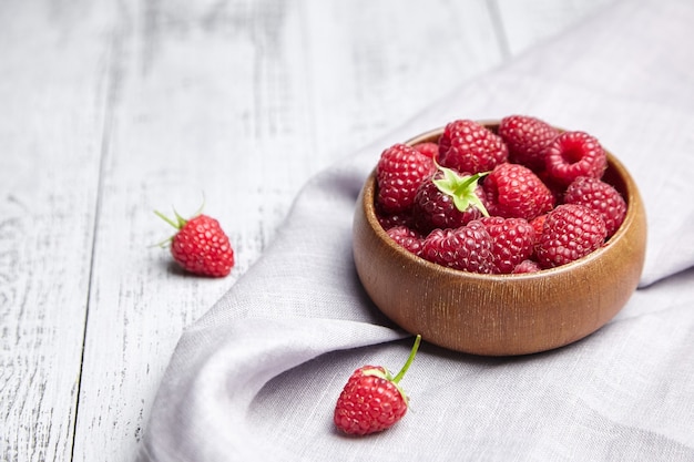 Fresh raspberries in wooden bowl on gray table with linen napkin