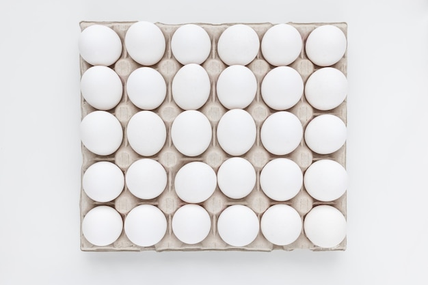 Fresh raw 30 pack of large white eggs in cardboard on white background Consumerism egg production organic healthy bio product and Easter holiday concept Top view of thirty eggs copy space