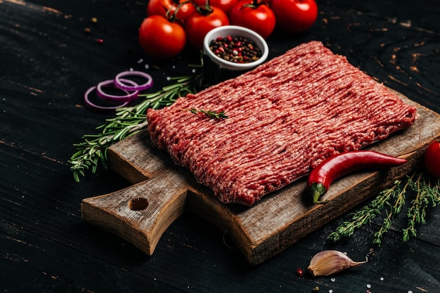 Fresh Raw Beef Minced Meat with herbs and rosemary on wooden board on a dark background banner menu recipe place for text top view