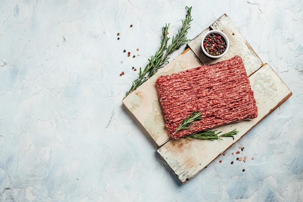 Fresh Raw Beef Minced Meat with herbs and rosemary on wooden board on a light background banner menu recipe place for text top view