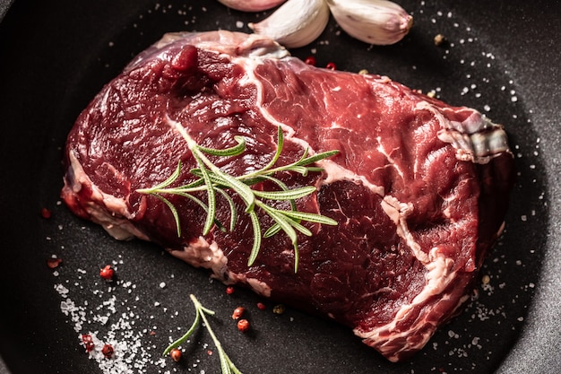 Fresh raw beef Ribe Eye steak in teflon pan with rosemary, garlic, salt and pepper.