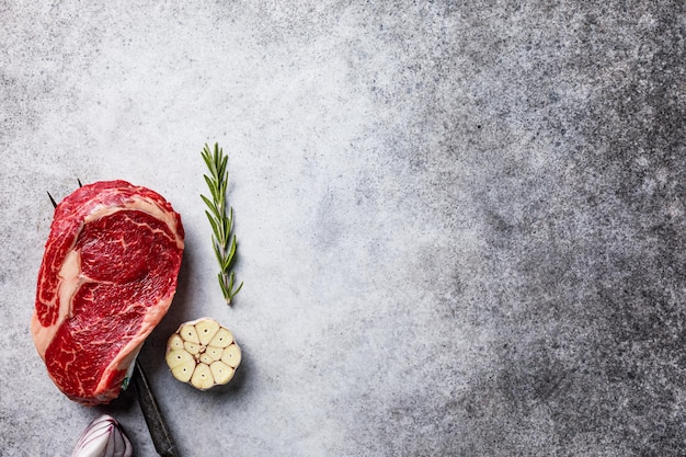 Fresh raw beef ribeye steak on fork with spices on stone board