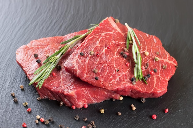 Fresh raw beef steak with spice on black slate background