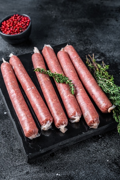 Fresh Raw butchers sausages in skins with thyme on marble board. Black background. Top view.