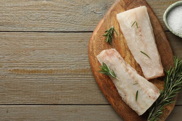 Photo fresh raw cod fillets salt and rosemary on wooden table flat lay space for text