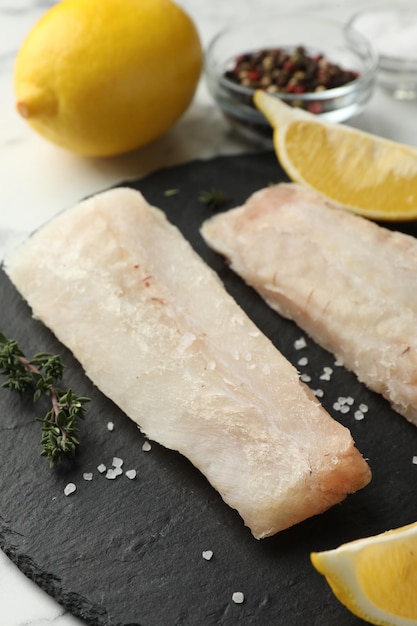 Photo fresh raw cod fillets spices and lemon on white table closeup