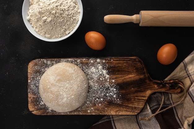 Fresh raw dough for bread or pizza with eggs on a dark with dusting of flour.