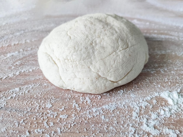 Fresh raw dough on wooden table covered with flour top view