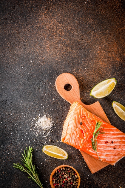 Fresh raw fish salmon, steak fillet, with spices, lime, rosemary, salt, on a dark rusty scene top view