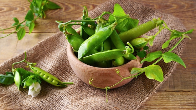 Fresh raw green peas beans  in light wooden bowl on canvas jute cloth vintage wooden background, horizontal, selective focus. Healthy eating antioxidant nutrition concept.