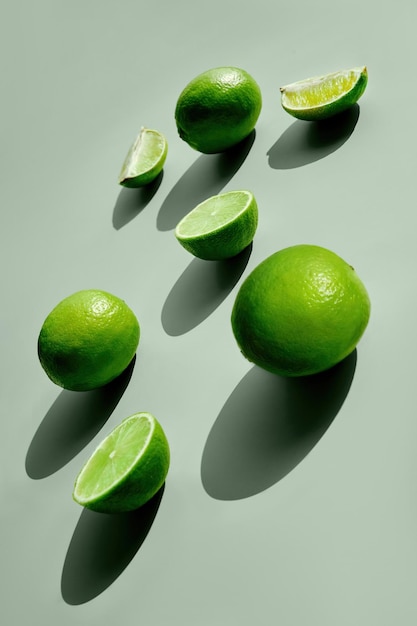 Fresh raw lime fruit on light green background Creative composition sun light long shadows Vertical format