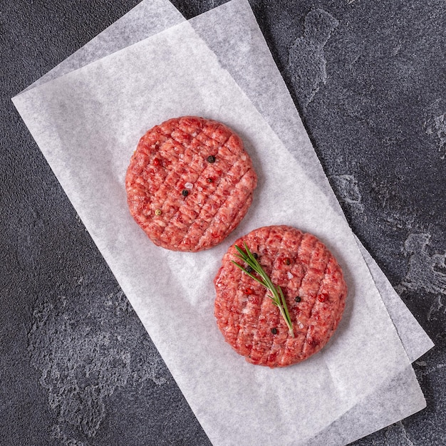 Fresh raw meat burger cutlet with herbs and spices on the black stone board