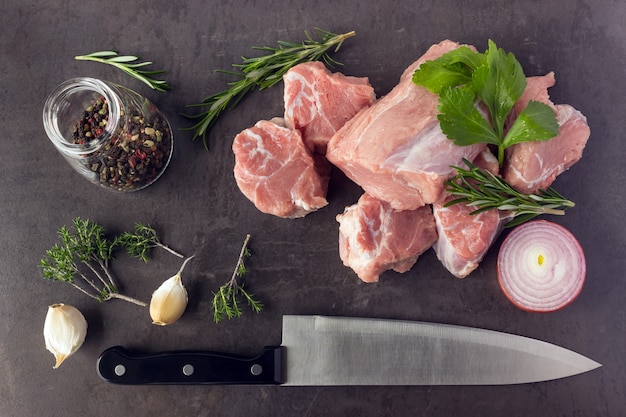 Fresh raw meat with herbs, spices and a butcher knife lies on the surface of a dark stone. Cooking concept. Top view