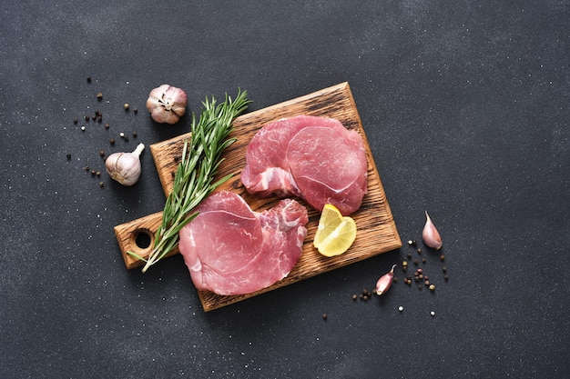 Fresh raw meat on a wooden board with rosemary and lemon on a black background pork steak