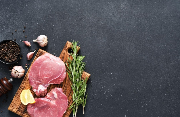 Fresh raw meat on a wooden board with rosemary and lemon on a black background pork