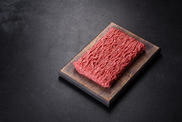 Fresh raw mince with spices and herbs on a dark concrete background