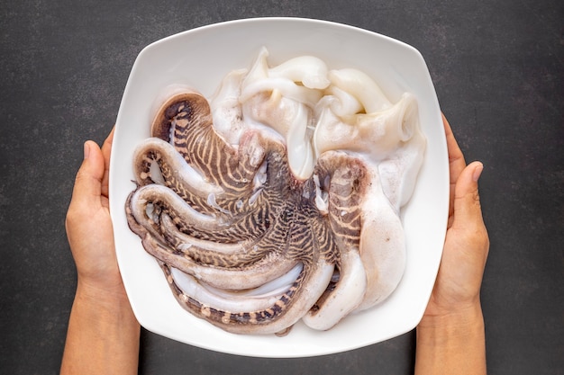 Fresh raw octopus in ceramic plate on dark tone texture background