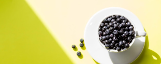 Fresh raw organic farm blueberry in white cup on yellow kitchen background copy spaceSummer seasonal natural vitamines and antioxidants Healthy diet and nutrition concept