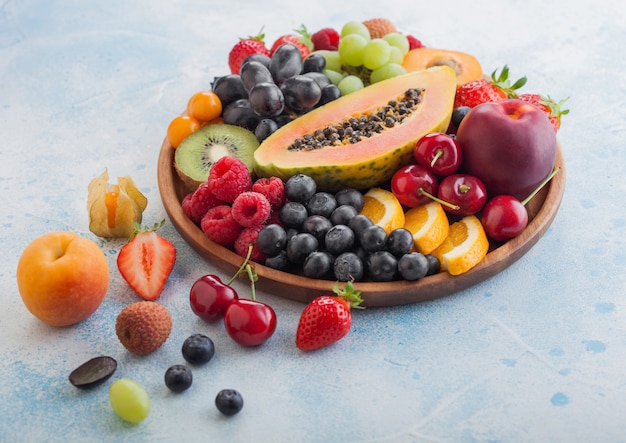 Fresh raw organic summer berries and exotic fruits in round wooden plate 