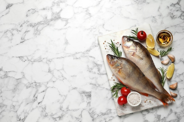 Fresh raw perches and ingredients on white marble table flat lay with space for text River fish