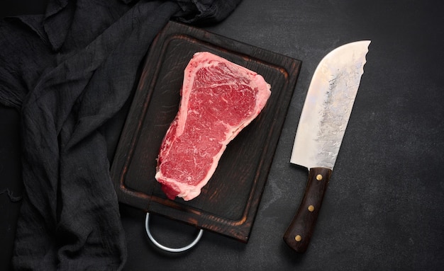 Fresh raw piece of beef meat striploin steak on a black background top view Marbled piece of meat