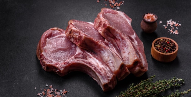 Fresh raw pork meat on the ribs with spices and herbs on a wooden cutting board on a dark concrete background