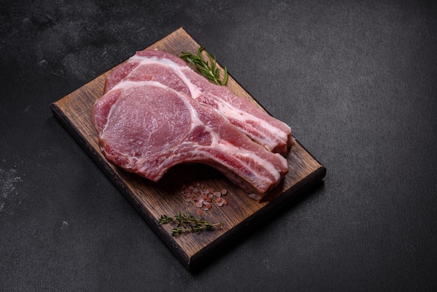 Fresh raw pork meat on the ribs with spices and herbs on a wooden cutting board on a dark concrete background