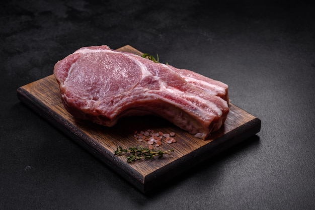 Fresh raw pork meat on the ribs with spices and herbs on a wooden cutting board on a dark concrete background