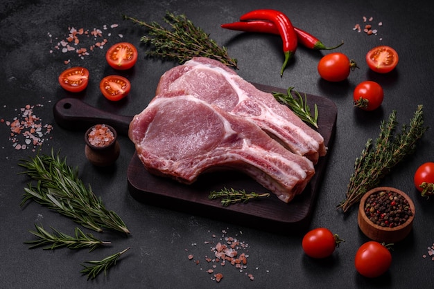 Fresh raw pork meat on the ribs with spices and herbs on a wooden cutting board on a dark concrete background