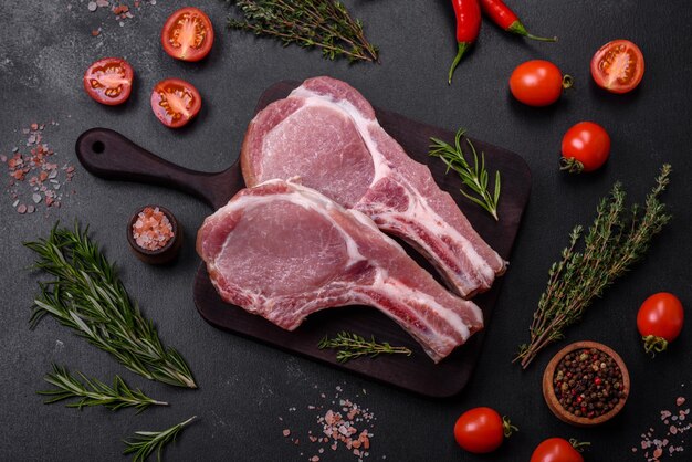 Fresh raw pork meat on the ribs with spices and herbs on a wooden cutting board on a dark concrete background