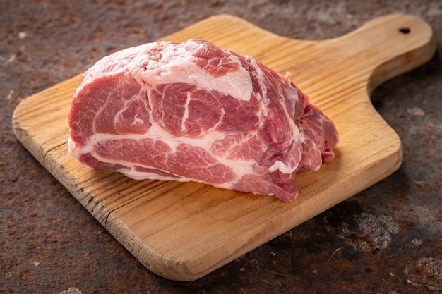 Fresh raw pork neck meat fillet in wooden cutting board on rusty texture background, ingredient for chop steak