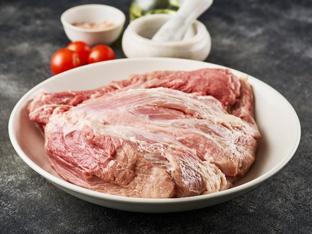 Fresh raw pork shoulder with ingredients for marinade: pepper, salt, olive oil, rosemary, garlic