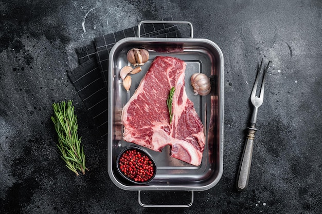 Fresh Raw porterhouse T bone beef meat Steak in steel tray with herbs Black background Top view