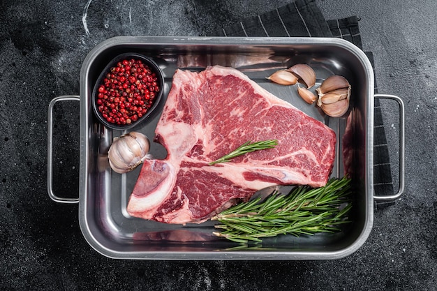 Fresh Raw porterhouse T bone beef meat Steak in steel tray with herbs Black background Top view