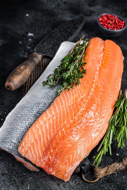 Fresh raw salmon fillet fish on cutting board with knife. Black background. Top view.