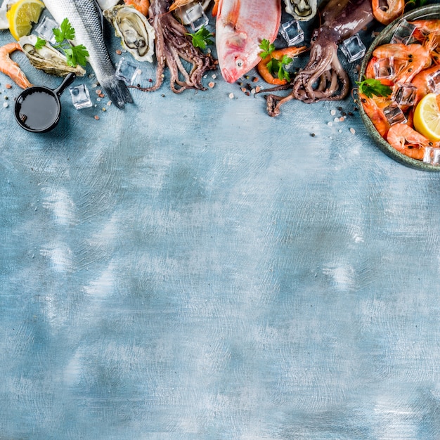 Fresh raw seafood squid shrimp oyster mussels fish with spices of herbs lemon on a light blue table top view