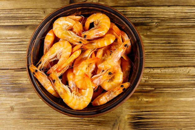 Fresh raw shrimps in a ceramic bowl on a wooden table Top view