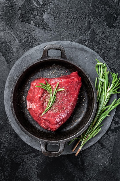 Fresh Raw sirloin rump steak in a skillet with herbs Black background Top view