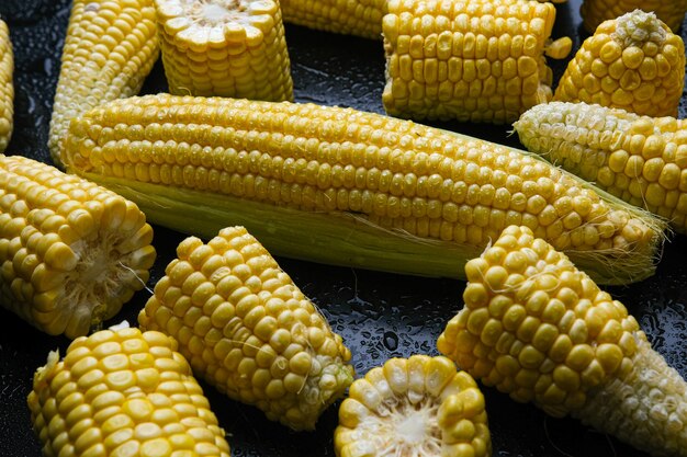 Fresh raw sweet corn cobs on black background. close-up.