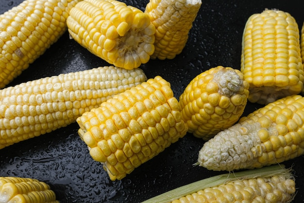 Fresh raw sweet corn cobs on black background. close-up.