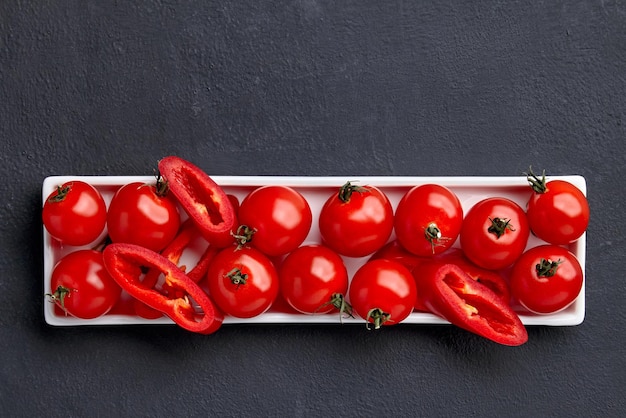 Fresh raw washed cherry tomatoes and paprika slices on a white oblong dish on a black concrete table