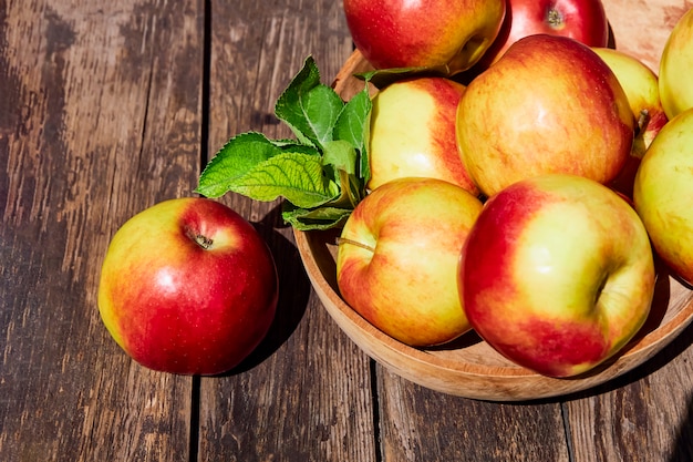 Fresh red apples with green leaves on a wooden old table.