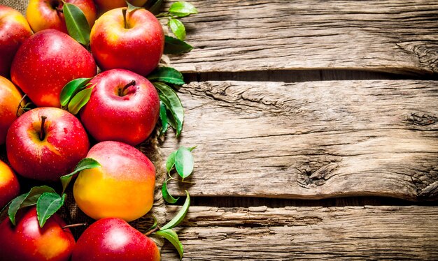 Fresh red apples with green leaves on wooden table. On wooden background. Free space for text .